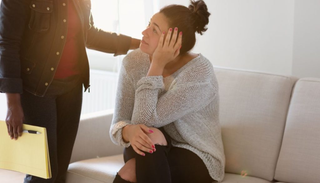 Woman sitting on a couch with her head resting on her hand as therapist offers support.
