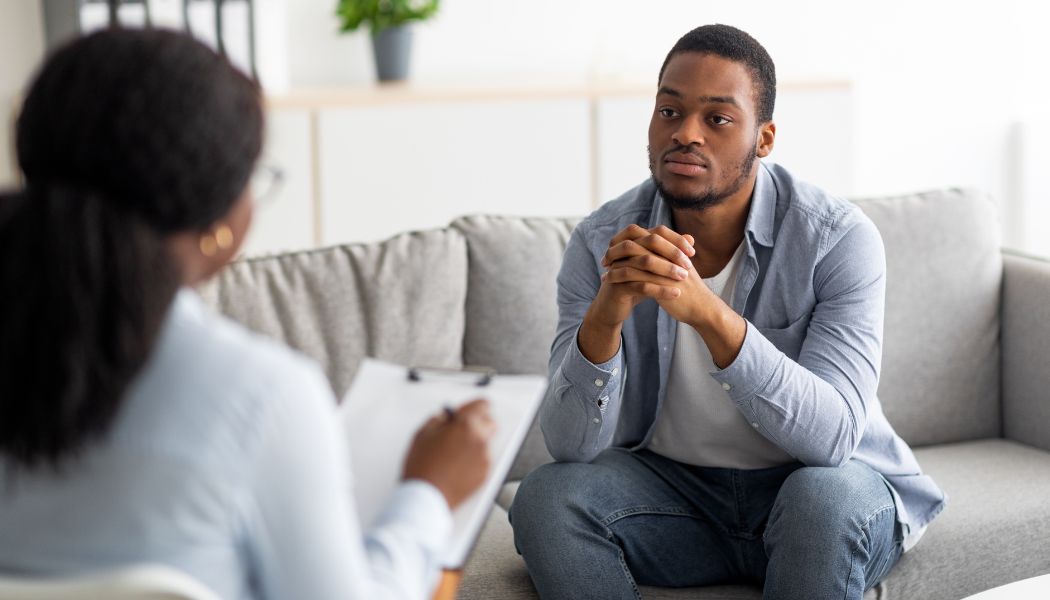 Man sitting on a couch attentively listening to a therapist during an evaluation