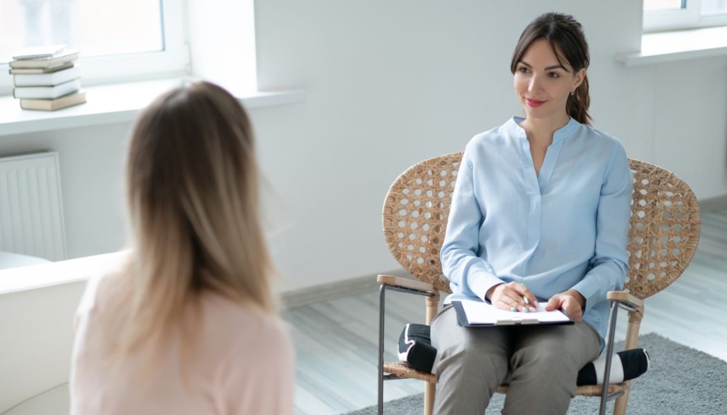 Therapist smiling and taking notes while speaking with a seated patient in an office