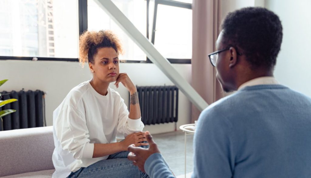 Woman sitting on a couch listening thoughtfully to a therapist during a discussion
