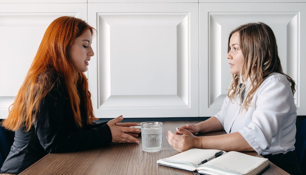 Two women sitting across from each other at a table having a serious conversation.