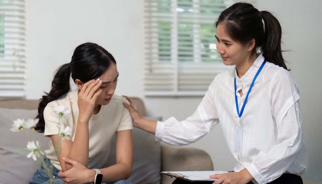 Female therapist comforting a woman holding her head while sitting on a couch during a session.