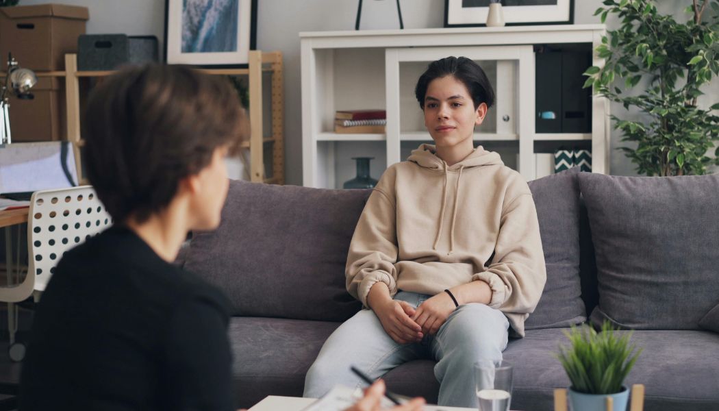 Teenager sitting on a couch talking with a therapist during a session.